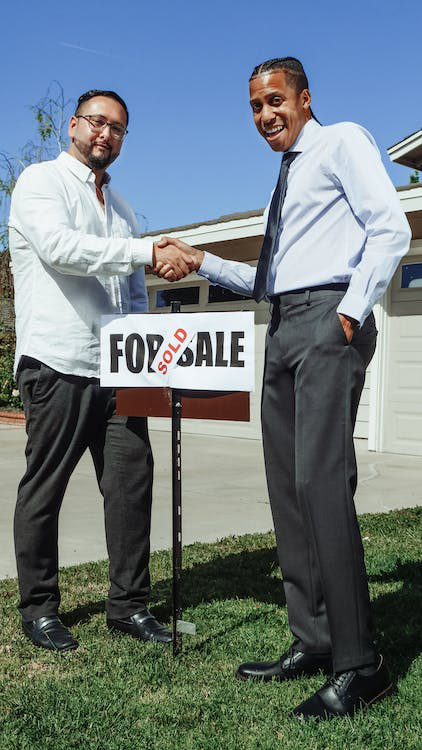 People shaking hands in front of a “sold” signage