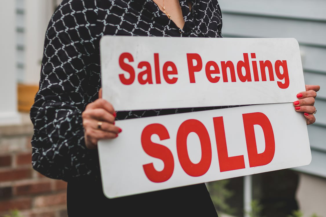 Woman holding signages for “sale pending” and “sold”